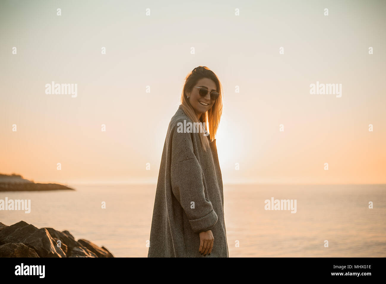 Ritratto di donna che indossa gli occhiali da sole e cappotto invernale guardando la telecamera sorridendo, vista laterale, Odessa, Odeska, Oblast di Ucraina Foto Stock