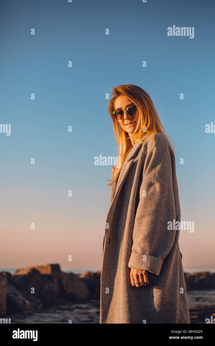 Ritratto di donna che indossa gli occhiali da sole e cappotto invernale guardando la telecamera sorridendo, vista laterale, Odessa, Odeska, Oblast di Ucraina Foto Stock