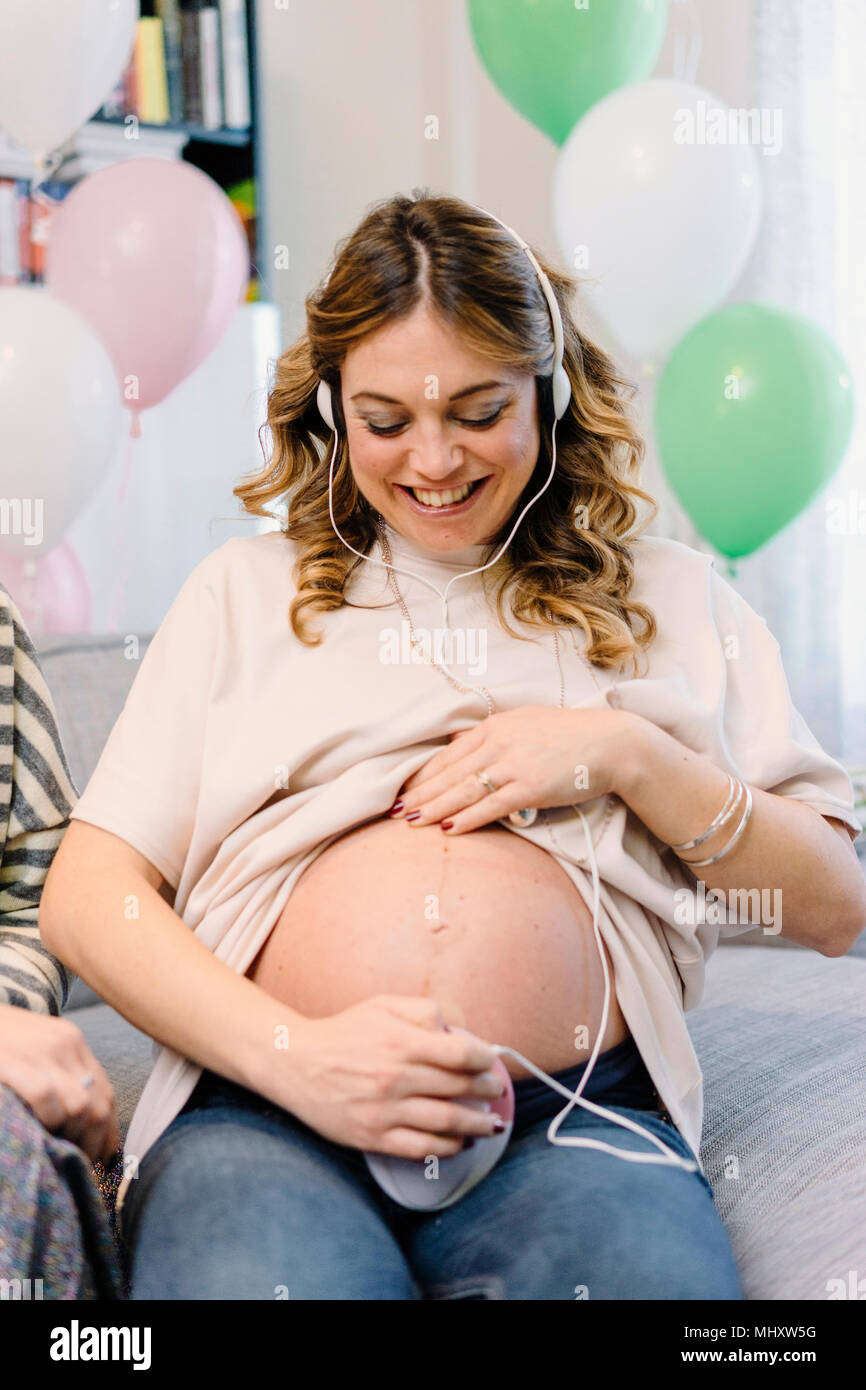 Donna incinta sul divano utilizzando prenatale di dispositivo di ascolto Foto Stock