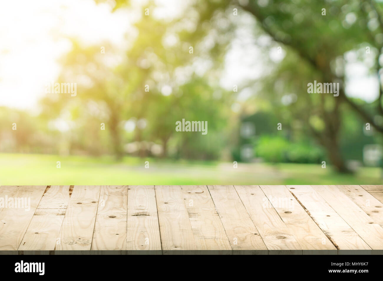 Svuotare tavolo in legno e defocalizzata bokeh di fondo e la sfocatura sullo sfondo di un giardino di alberi nella luce solare, display montage per prodotto. Foto Stock