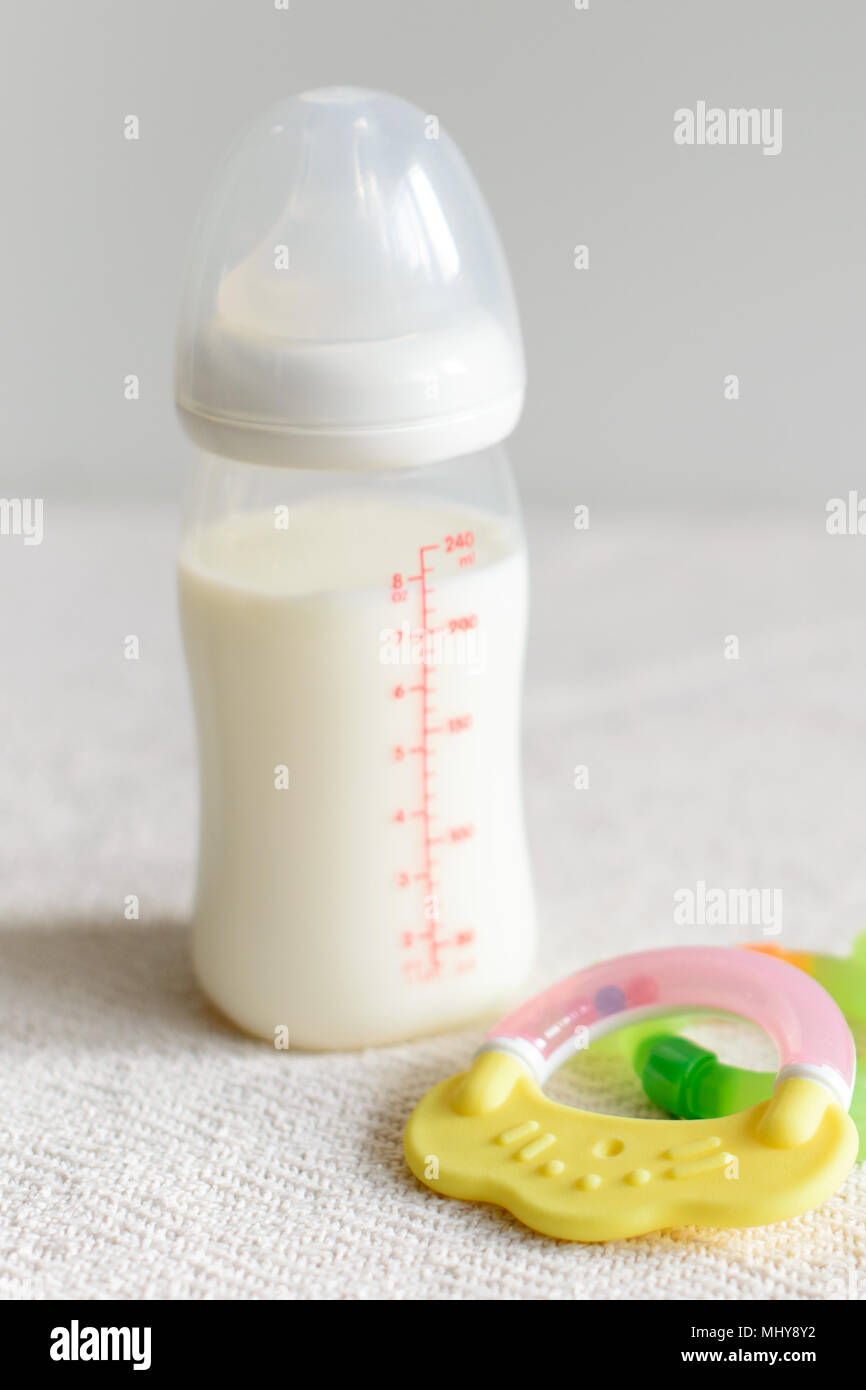 Bottiglia di latte per il bambino e giocattoli su sfondo sfocato Foto Stock