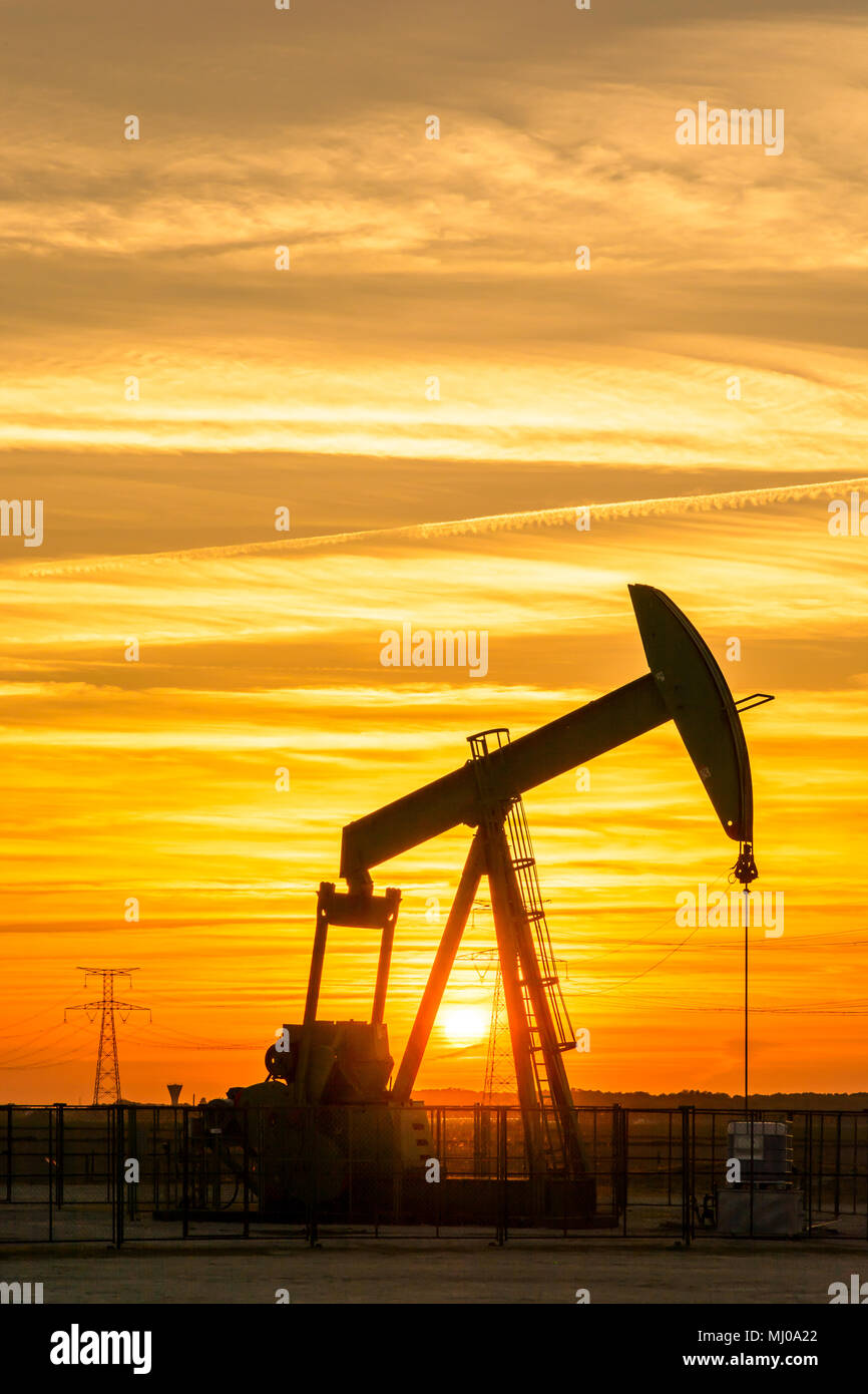 Pumpjack e le torri di trasmissione al tramonto simboleggiano la transizione ecologica. Un martinetto a pompa con tralicci elettrici e linea di alimentazione contro un cielo rosso. Foto Stock