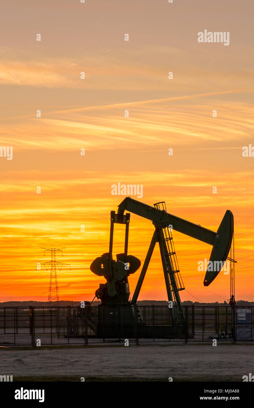 Pumpjack e le torri di trasmissione al tramonto simboleggiano la transizione ecologica. Un martinetto a pompa con tralicci elettrici e linea di alimentazione contro un cielo rosso. Foto Stock