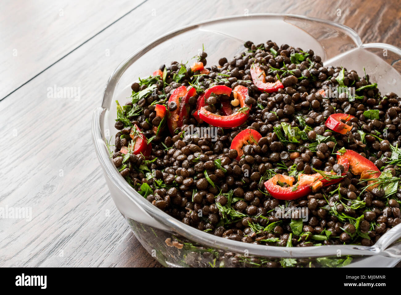 Nero insalata di lenticchie con peperoncino e prezzemolo nel recipiente di vetro. Foto Stock