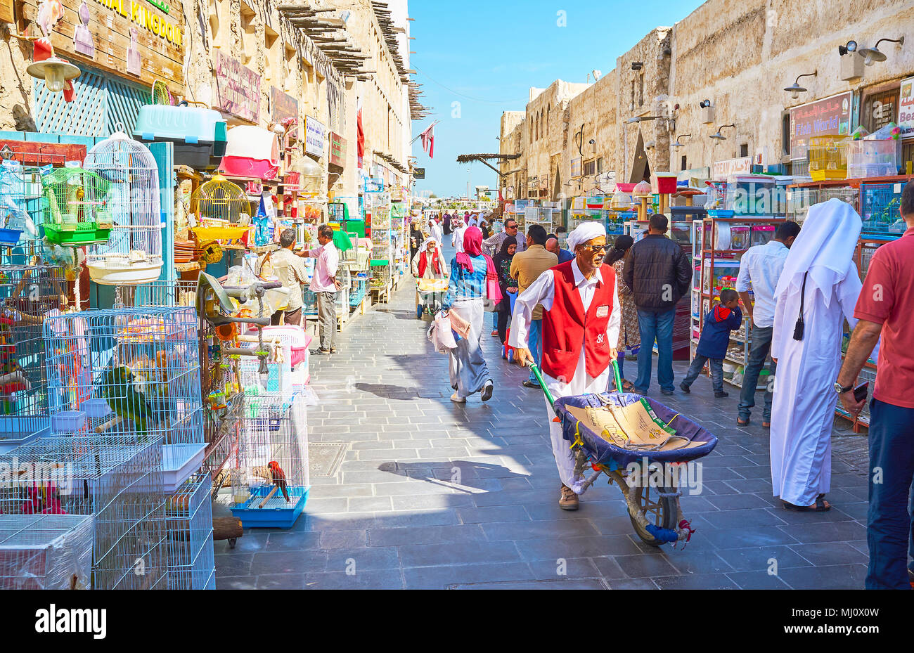 DOHA, Qatar - 13 febbraio 2018: Il portiere senior con carrello passeggiate lungo la strada affollata di uccelli mercato, pieno di gabbie con rumorosa uccelli e animali domestici, Foto Stock