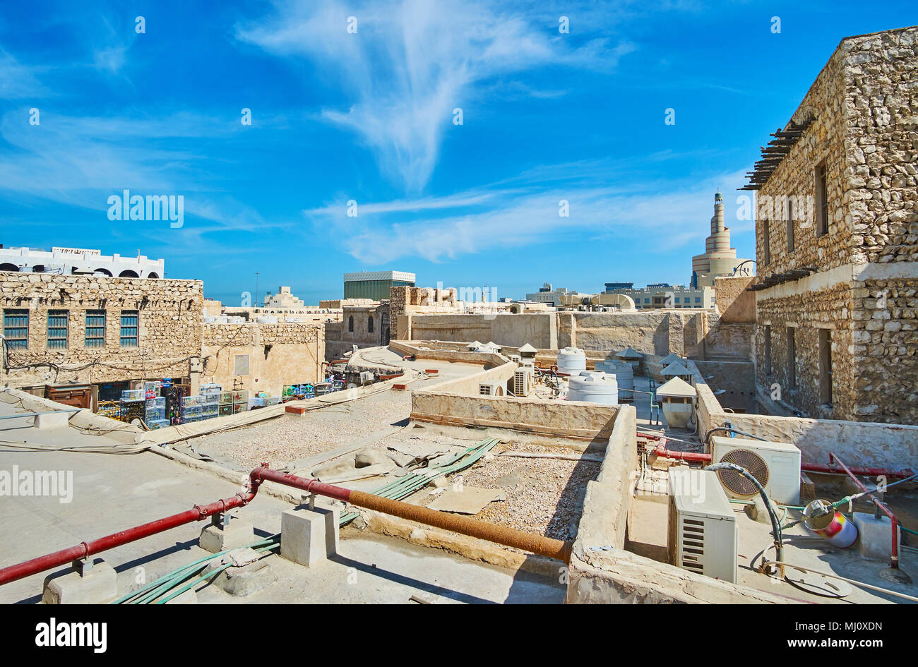 La passeggiata lungo i vecchi tetti di Souq Waqif con una vista sul minareto a spirale del Fanar moschea sullo sfondo, Doha, Qatar. Foto Stock