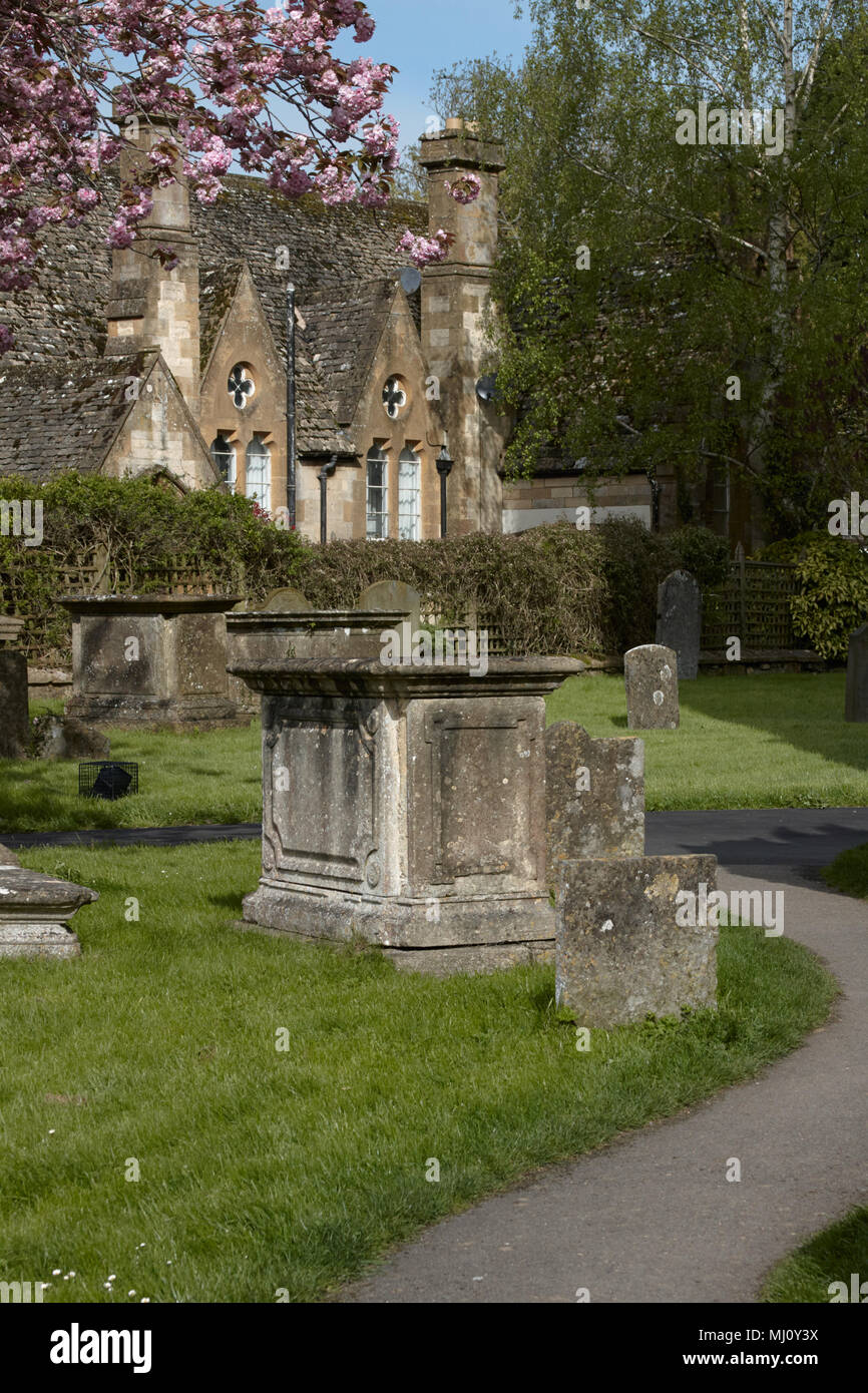 Sentiero del cimitero e la tomba nella motivazione di Winchcombe chiesa. Un Cotswold cottage in pietra in background. Foto Stock