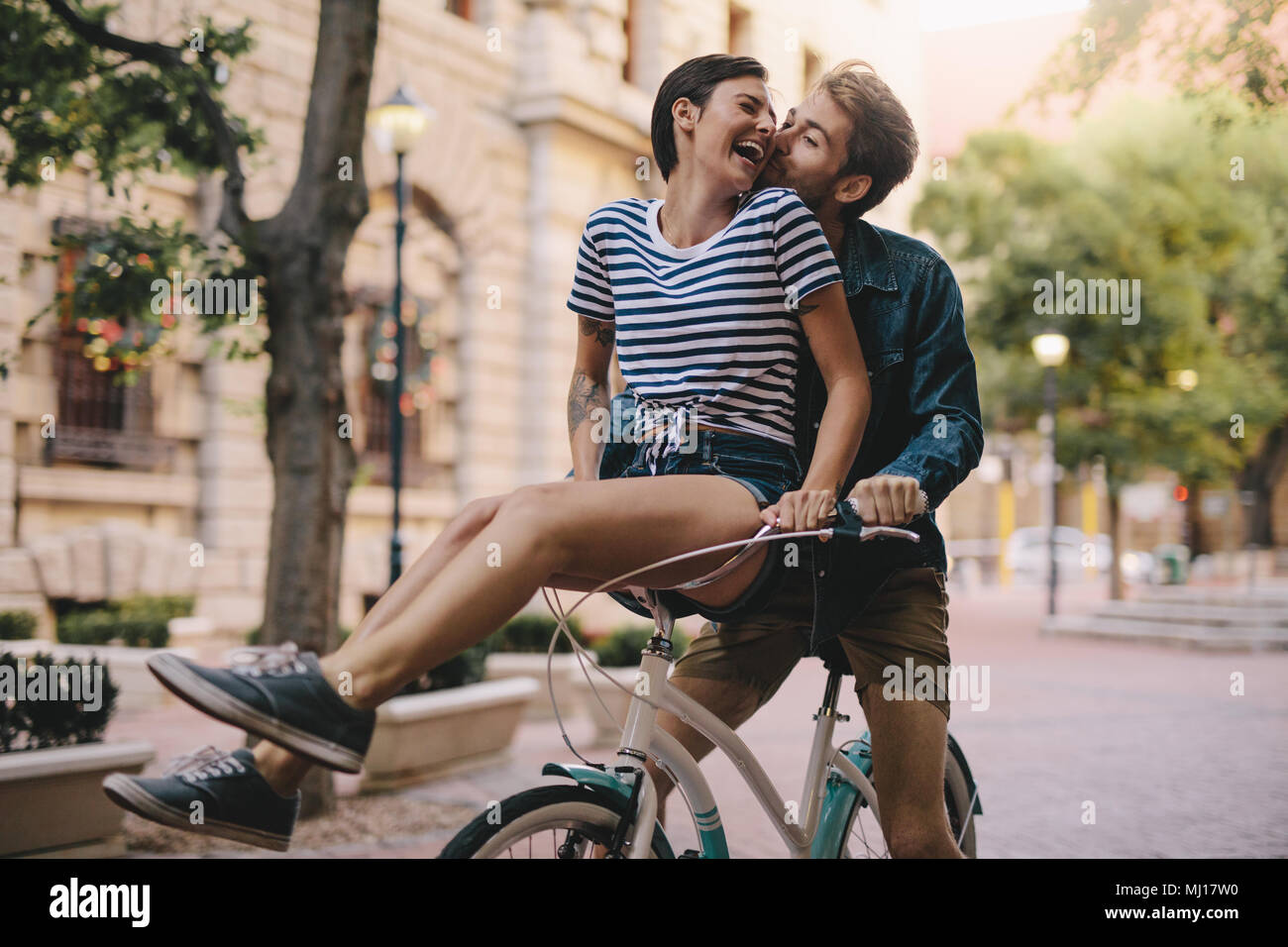 Ridendo donna seduta su fidanzati manubrio di bicicletta. Allegro giovane in sella a una moto insieme nella città di divertimento. Foto Stock