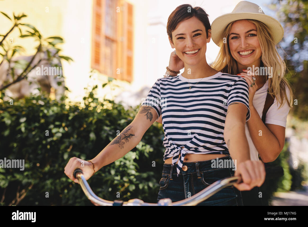 Donna sorridente escursioni in bicicletta con la sua amica sulla strada della citta'. Due giovani femmine in sella insieme su una bicicletta all'aperto e divertirsi. Foto Stock