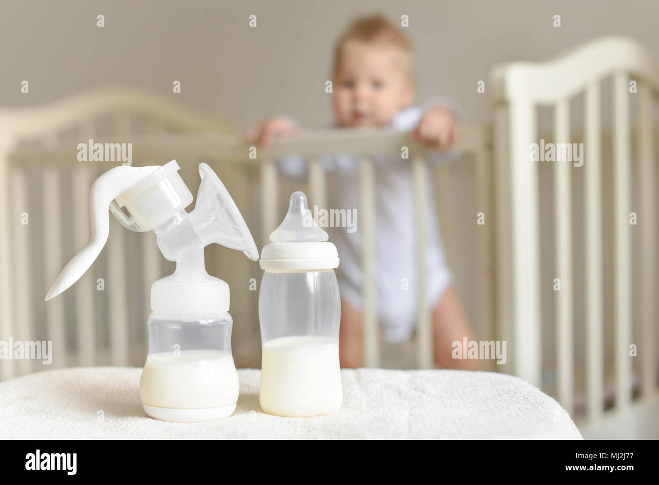 Tiralatte manuale e la bottiglia con il latte materno sullo sfondo del bambino più piccolo nel letto. Foto Stock