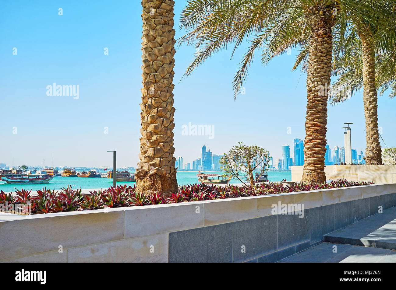 Rilassatevi sulla shaddy vicolo del museo parco con vista sul galleggiante barche Dhow e moderni grattacieli di vetro di Al Dafna district, Doha, Qatar. Foto Stock