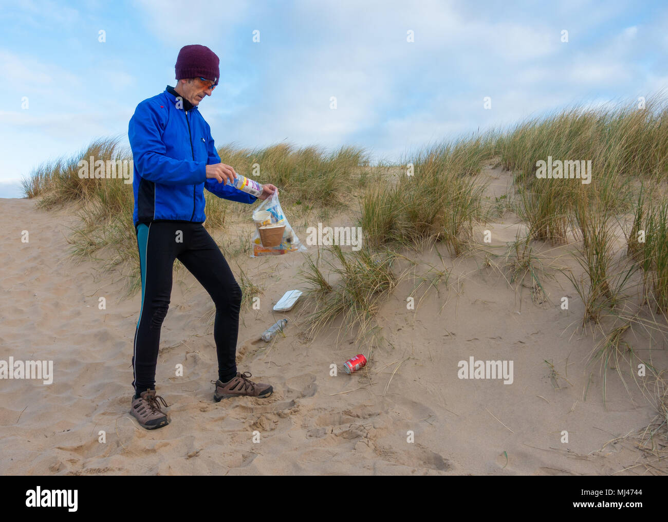 Un pareggiatore Plogging (prelievo di lettiera durante il jogging) sulla sua corsa mattutina attraverso le dune di sabbia.UK Foto Stock