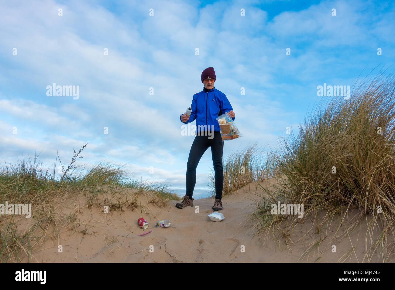 Un pareggiatore Plogging (prelievo di lettiera durante il jogging) sulla sua corsa mattutina attraverso le dune di sabbia.UK Foto Stock