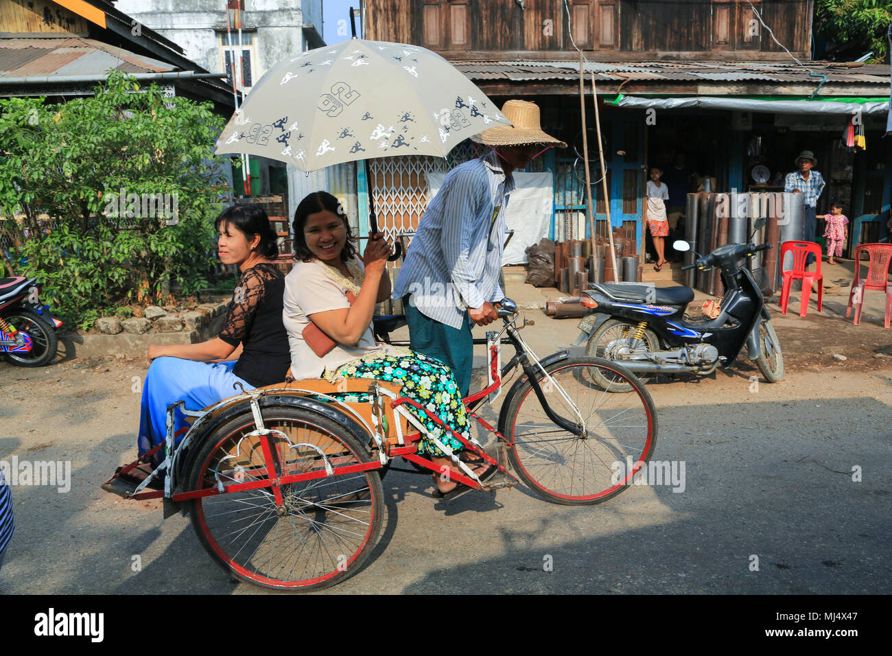 Un tri-shaw conducente di trasportare i suoi passeggeri e la loro shopping a Maubin, una città sul fiume Myitmaka, nel delta di Irrawaddy, Myanmar (Birmania). Foto Stock