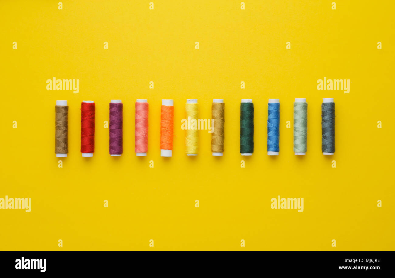 Colorate rocchetti di filo in una fila più luminoso dello sfondo giallo, sopra visualizza Foto Stock