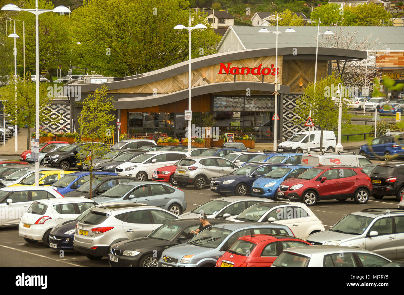 Ramo di Nando's pollo ristorante della catena in Talbot Green Shopping Park con le auto parcheggiate in primo piano Foto Stock