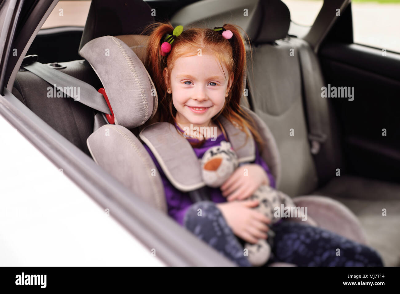 Baby poco i Capelli rossi ragazza sorridente mentre è seduto in un seggiolino per auto per bambino. Foto Stock