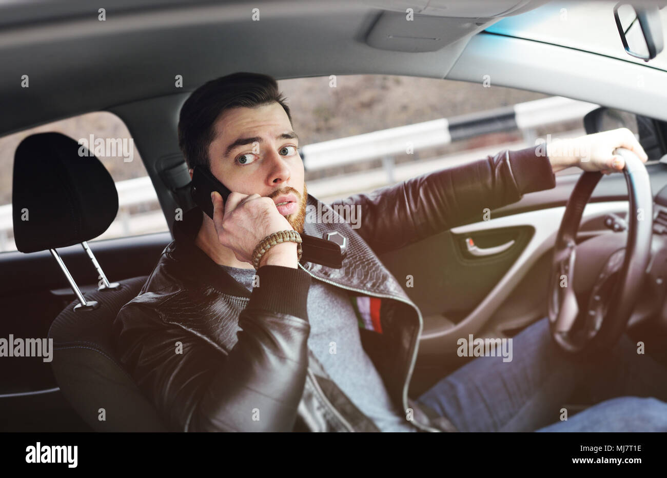 Giovane uomo che parla al telefono mentre si è alla guida di un veicolo Foto Stock