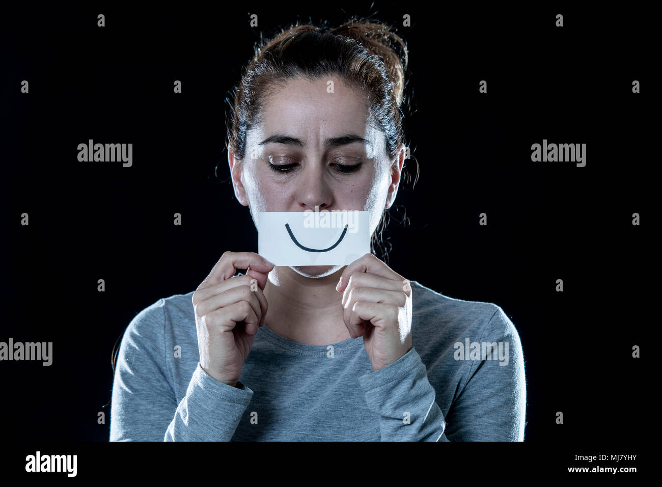 Giovane bella triste e depresso donna latina che copre la sua faccia triste con un foglio di carta tagliato fuori faccia felice in una depressione sul concetto isolato backgrou nero Foto Stock