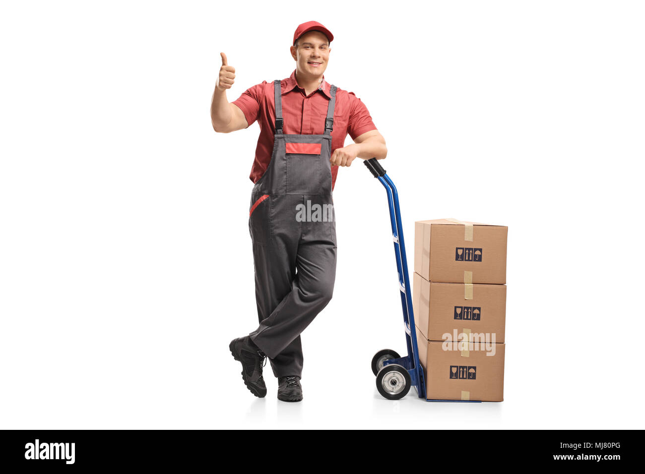 A piena lunghezza Ritratto di un mover appoggiato su di un carrello di caricamento scatole con la realizzazione di un pollice in alto gesto isolato su sfondo bianco Foto Stock
