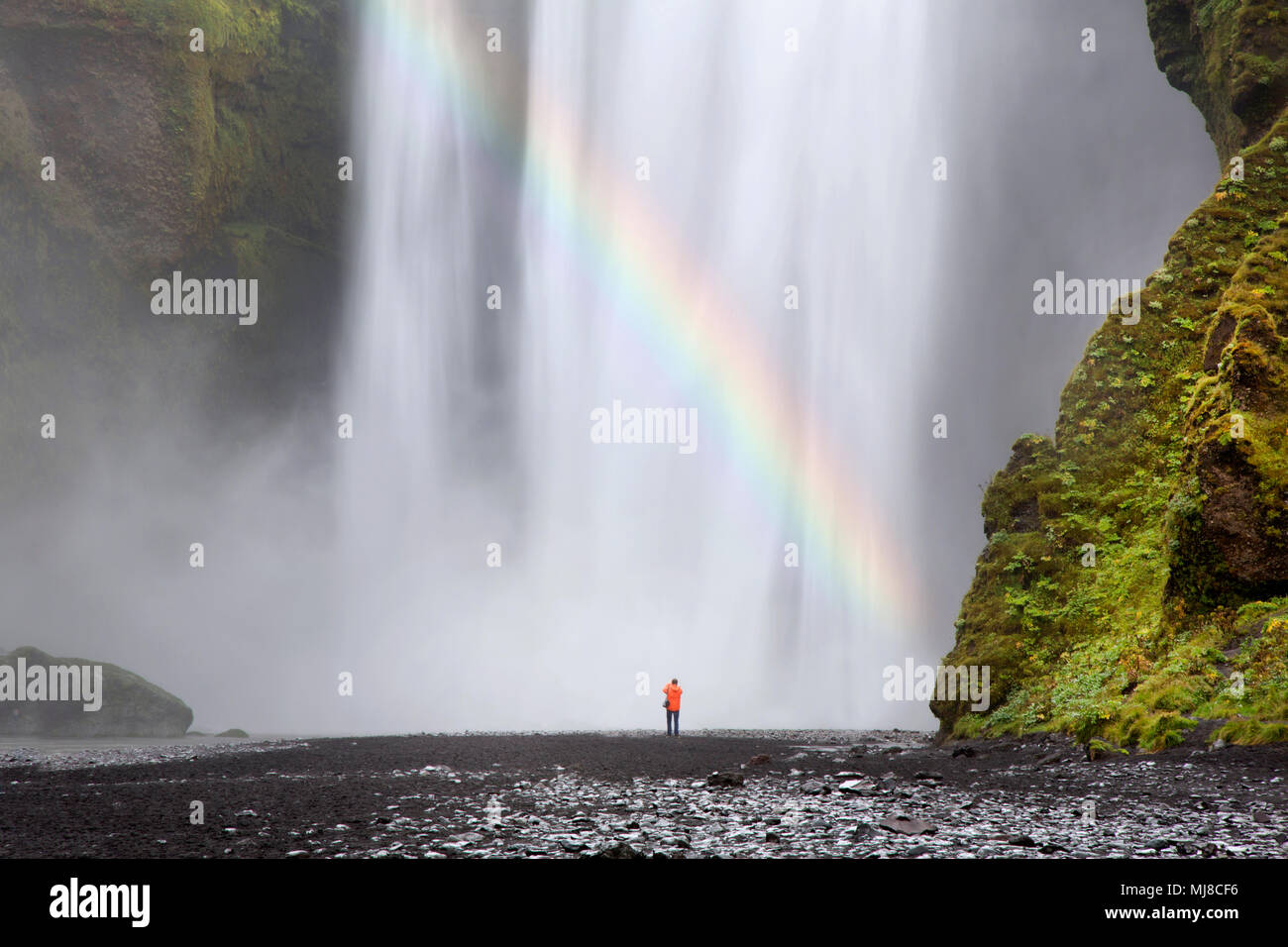 Vista posteriore della persona in piedi al piede della cascata, moss-coperta di rocce e cascate. Foto Stock