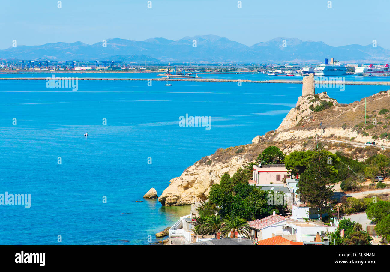 Una vista della costa di Sant Elia a Cagliari, Sardegna, evidenziando il prezzemolo torre sulla destra e il porto di Cagliari in background Foto Stock
