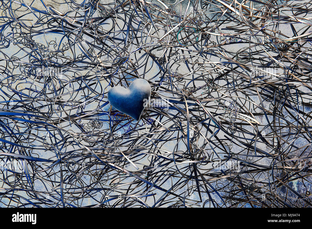 Un blu scuro cuore al centro di un groviglio di i ritagli di carta su uno sfondo di ardesia. Foto Stock