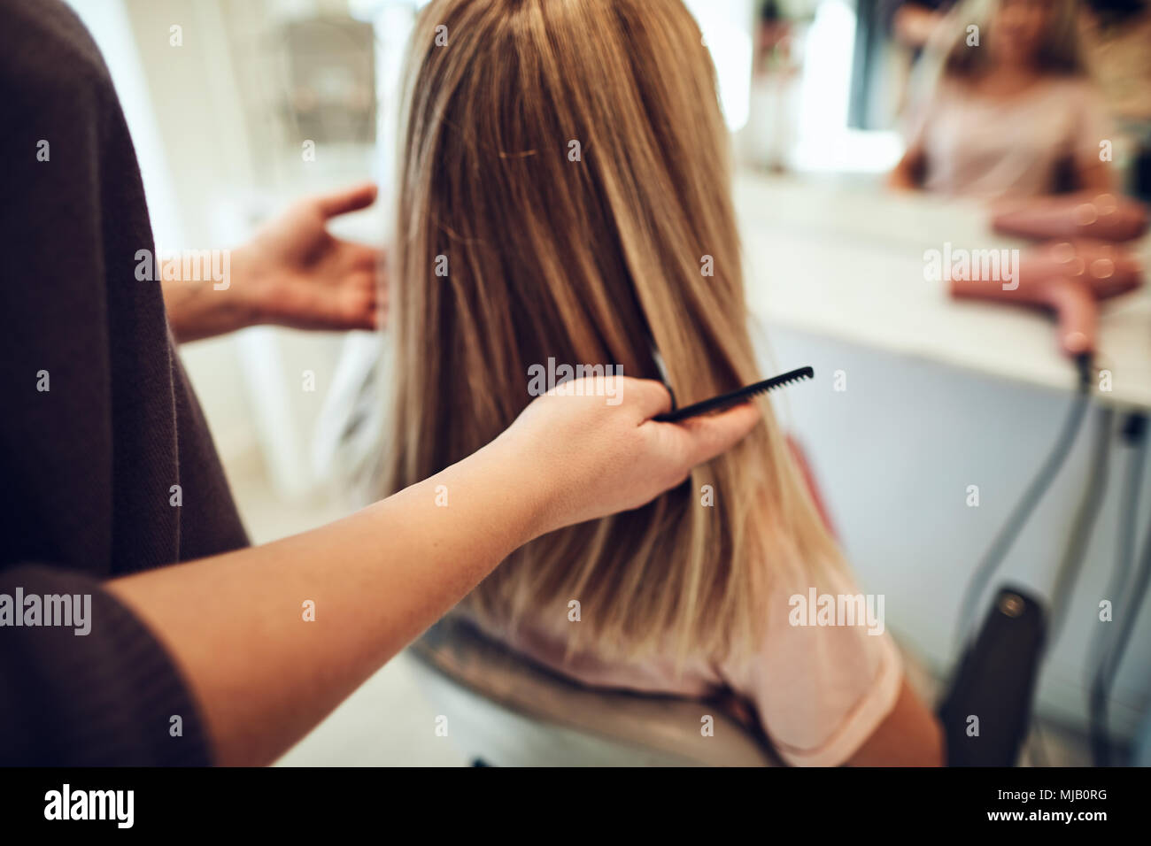 Donna bionda seduto in una sedia salone avente il suo stile di capelli durante un appuntamento con il suo parrucchiere Foto Stock