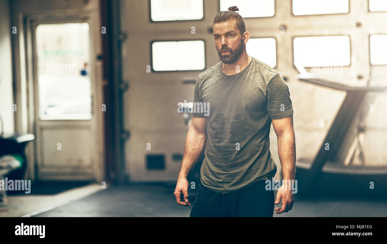 Montare e focalizzata giovane sportswear in piedi da solo in una palestra sudorazione dopo una sessione di allenamento Foto Stock