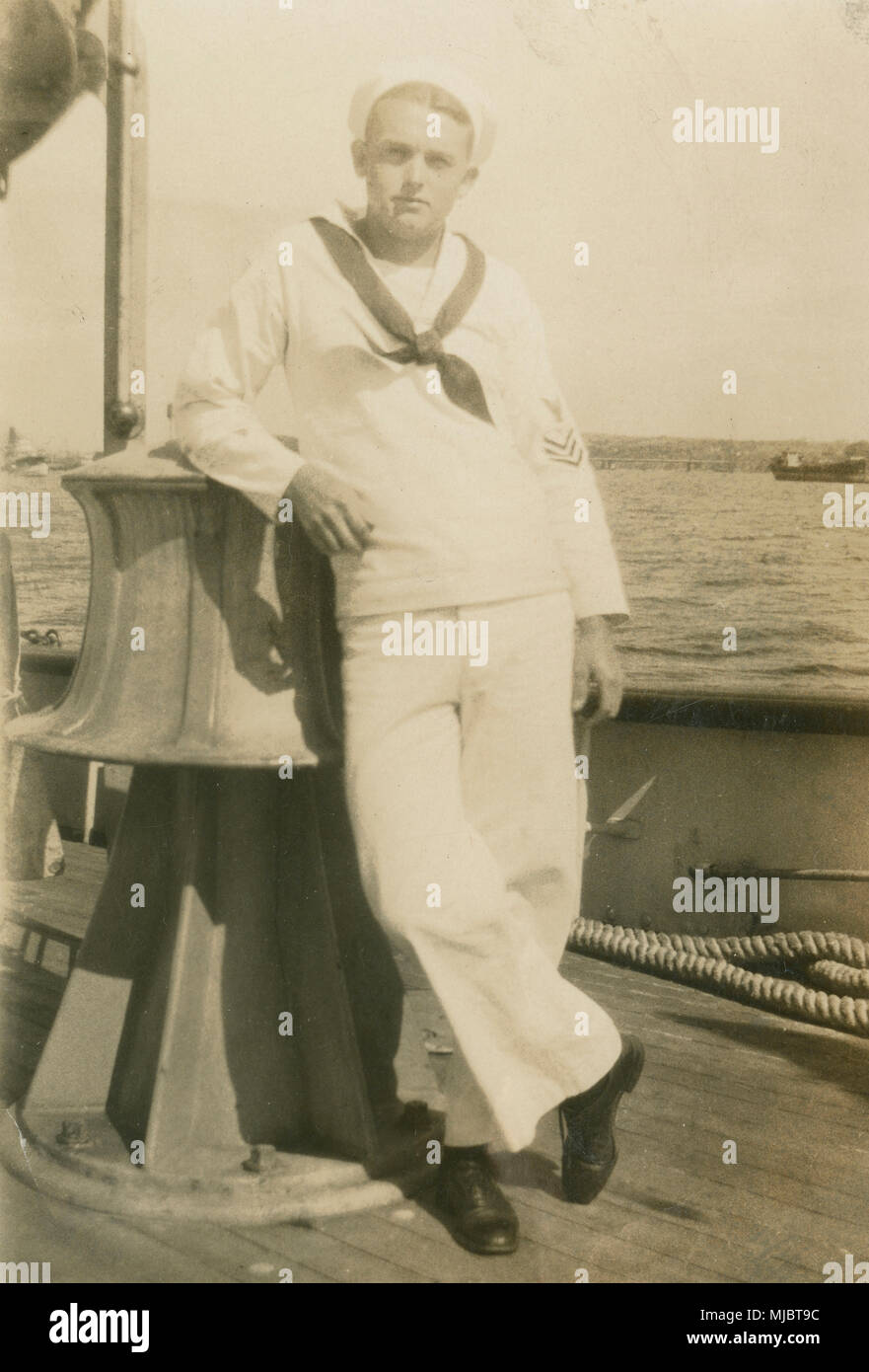 Antique c1922 fotografia, visualizzare a bordo della nave cavo USCG Pequot. Un marinaio in una US Coast Guard abito bianco uniforme, poggiando su quello che sembra essere il grande argano elettrico sul ponte. Fonte: originale stampa fotografica. Foto Stock
