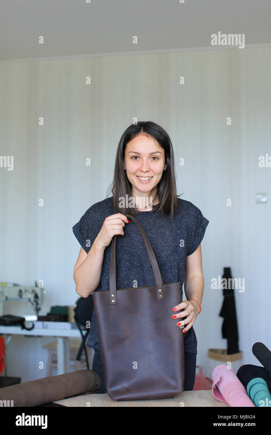 La donna caucasica rendendo in pelle marrone borsa a mano in atelier. Foto Stock