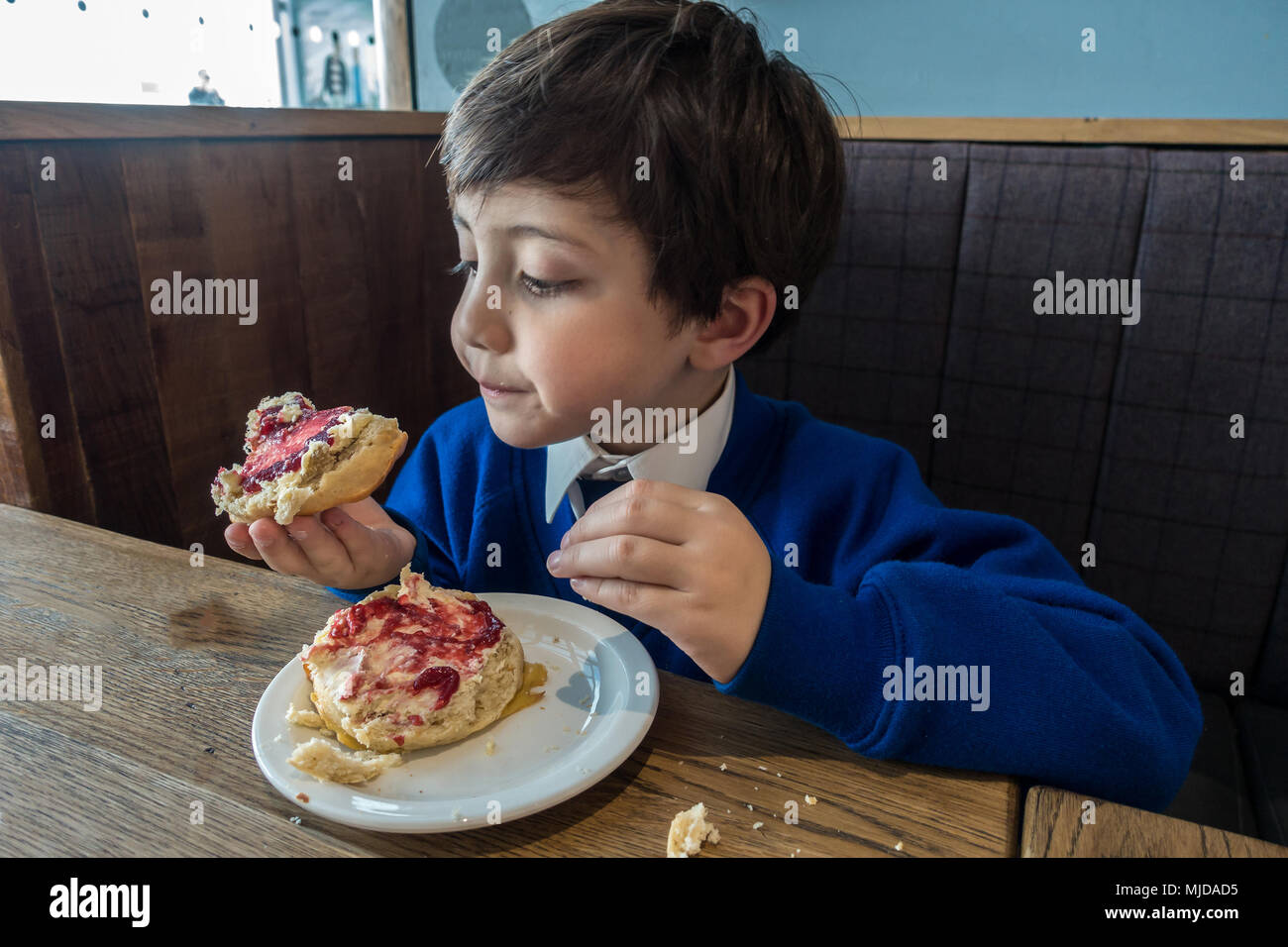 Un giovane ragazzo godendo di un frutto scone e rabboccato con clotted cream e confettura di lamponi. Foto Stock