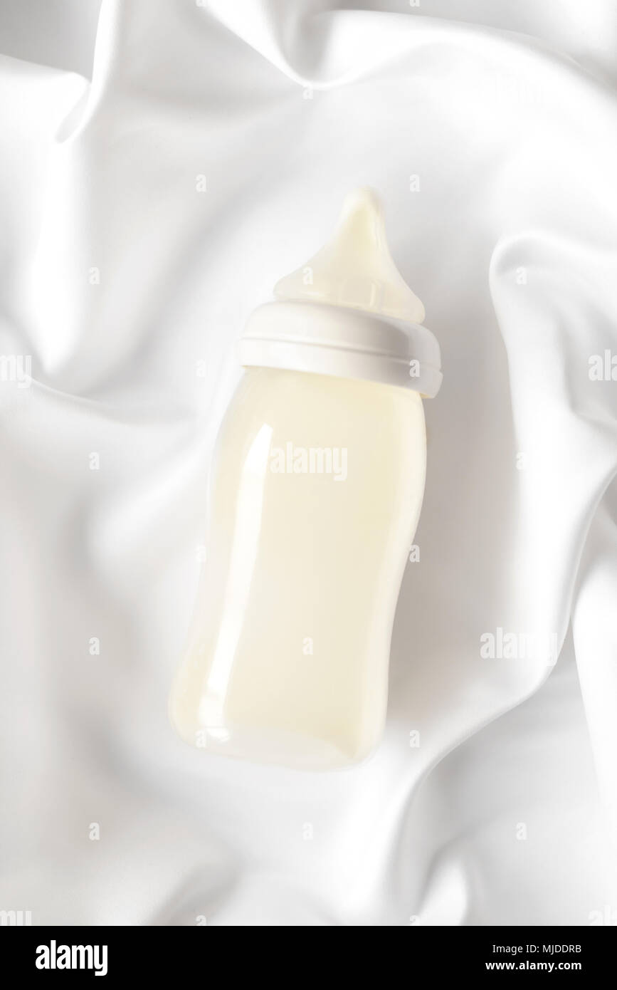 Bottiglia di latte per neonati su bianco raso di seta sfondo. La maternità e la cura del bambino concetto. Foto Stock