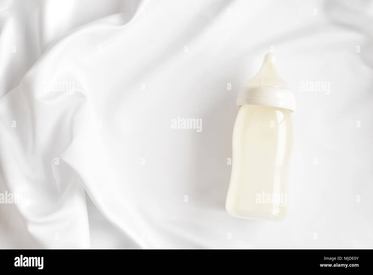 Bottiglia di latte per neonati su bianco raso di seta sfondo. Copia gratuita dello spazio. La maternità e la cura del bambino concetto. Vista dall'alto. Foto Stock