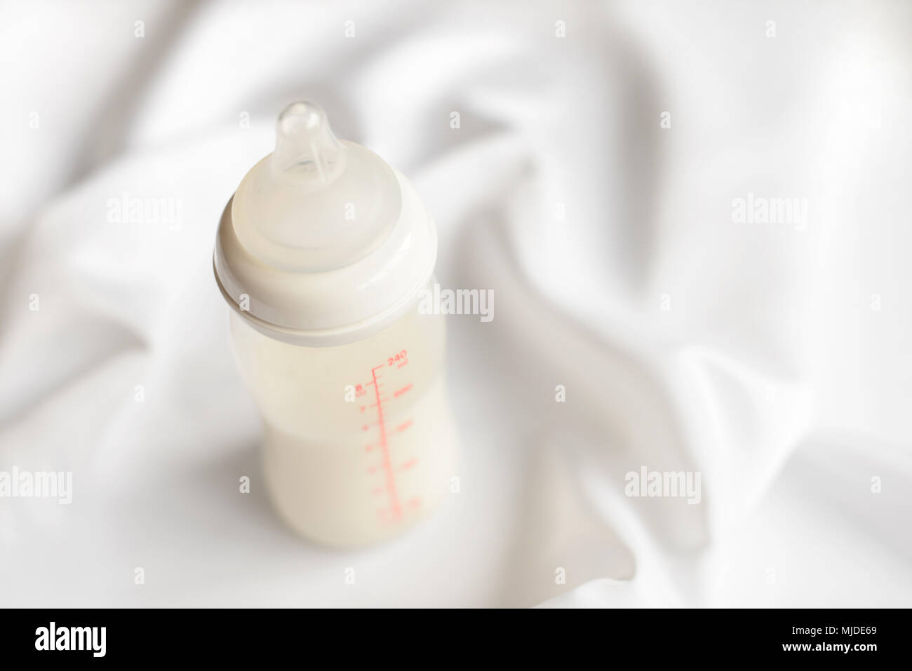 Bottiglia di latte per neonati su bianco raso di seta sfondo. Copia gratuita dello spazio. La maternità e la cura del bambino concetto. Foto Stock