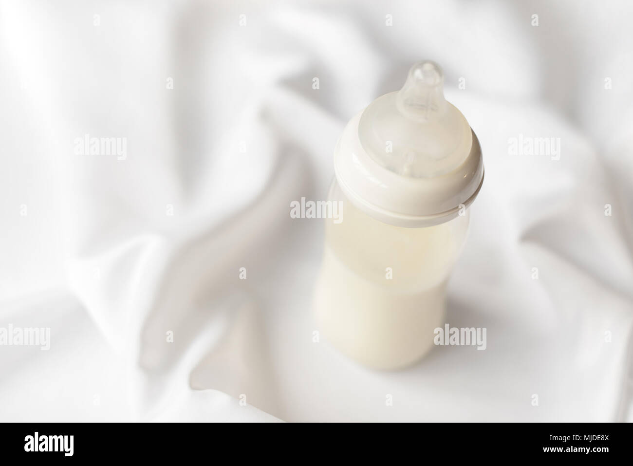 Bottiglia di latte per neonati su bianco raso di seta sfondo. Copia gratuita dello spazio. La maternità e la cura del bambino concetto. Foto Stock
