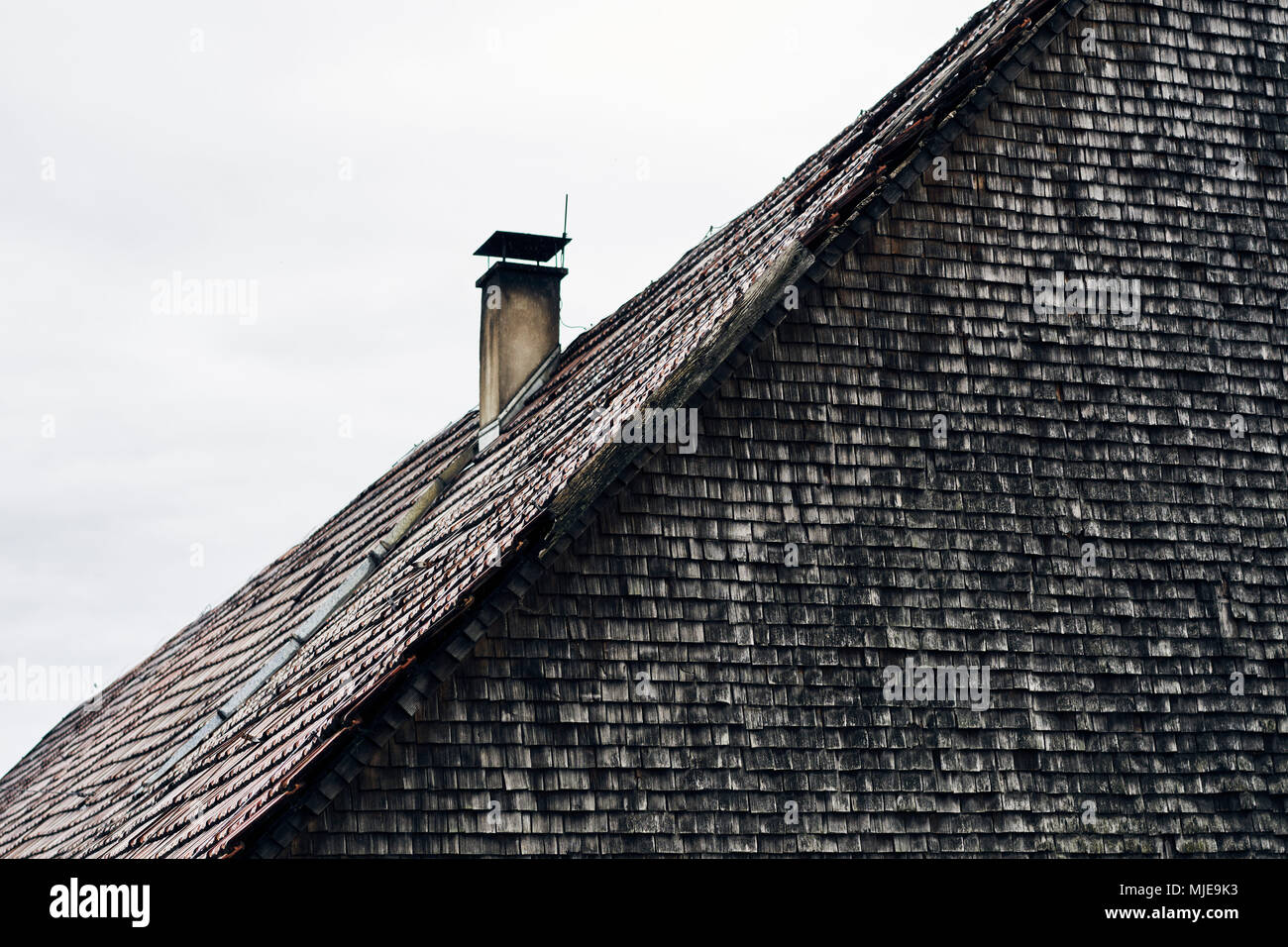 Tetto con mattoni e caminetto, vecchio le assicelle, grigio e stagionato su una casa di legno nella Foresta Nera Foto Stock