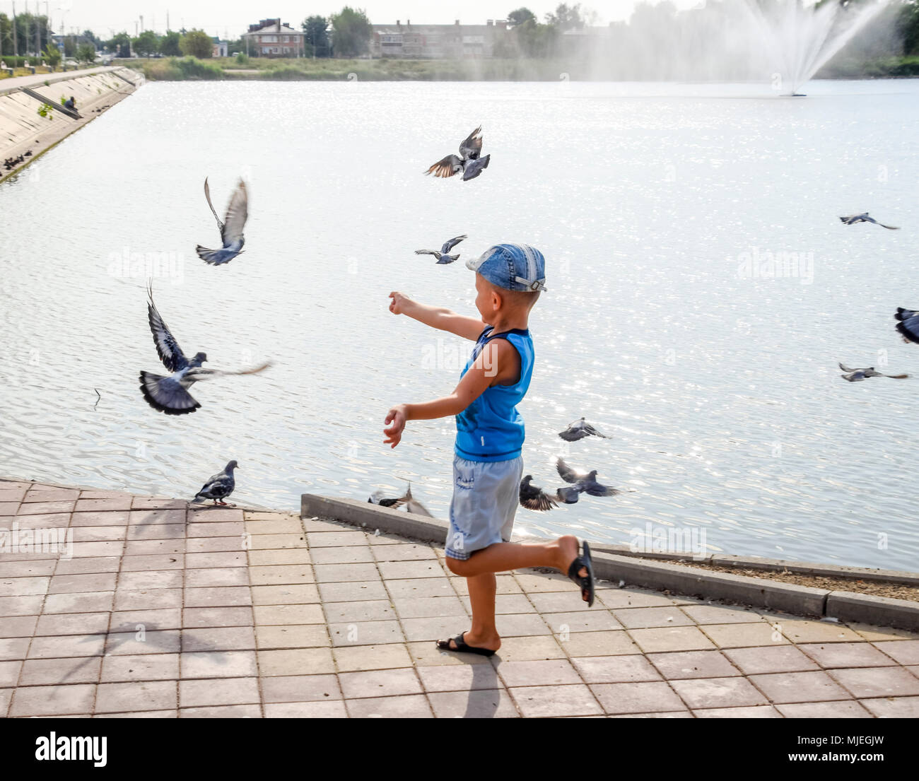 Il ragazzo corre lungo la passeggiata a lago e insegue i piccioni. Foto Stock