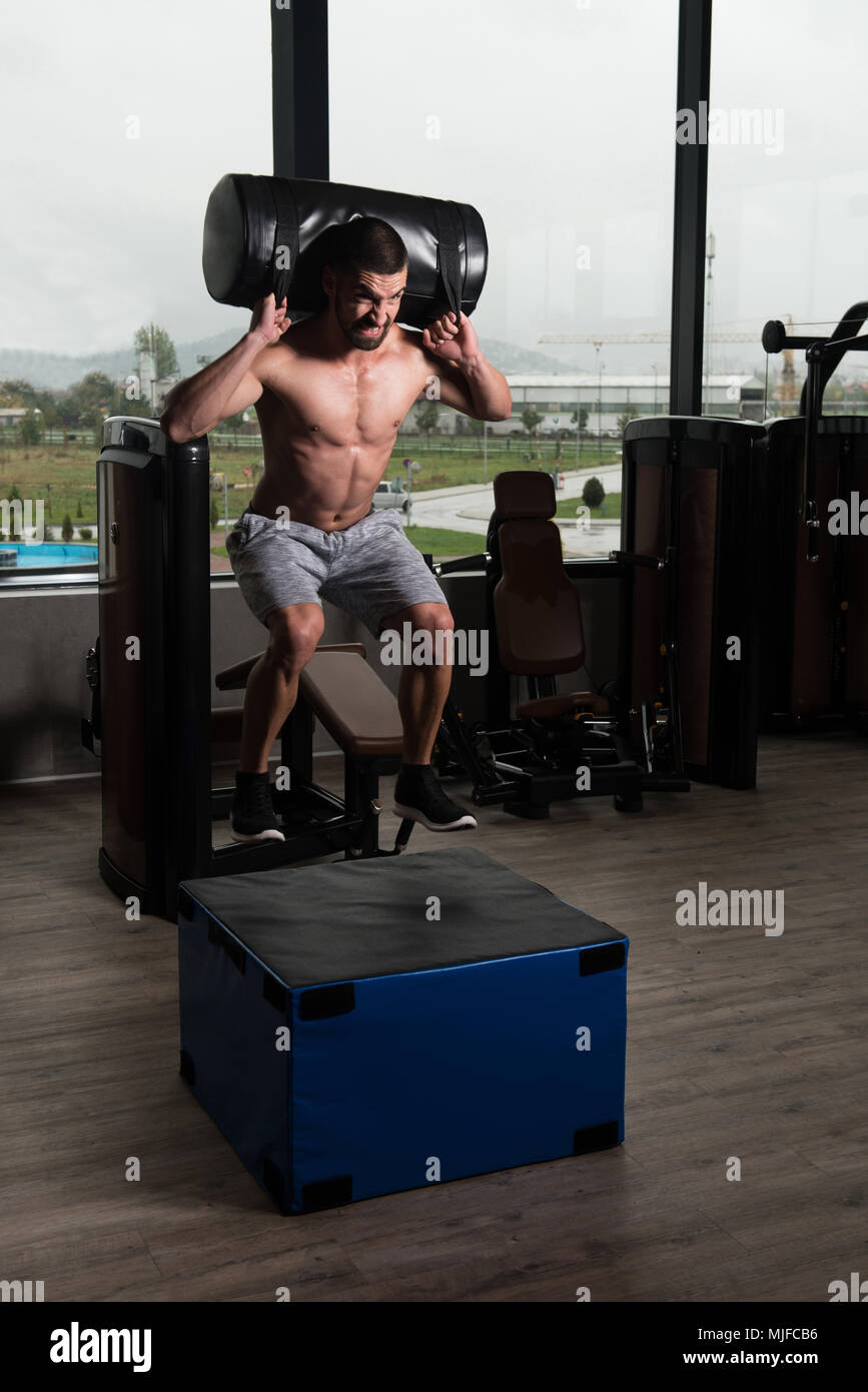 Montare il giovane uomo casella facendo saltare in uno stile palestra - atleta maschio è di eseguire la casella Salta in palestra con pesi Foto Stock