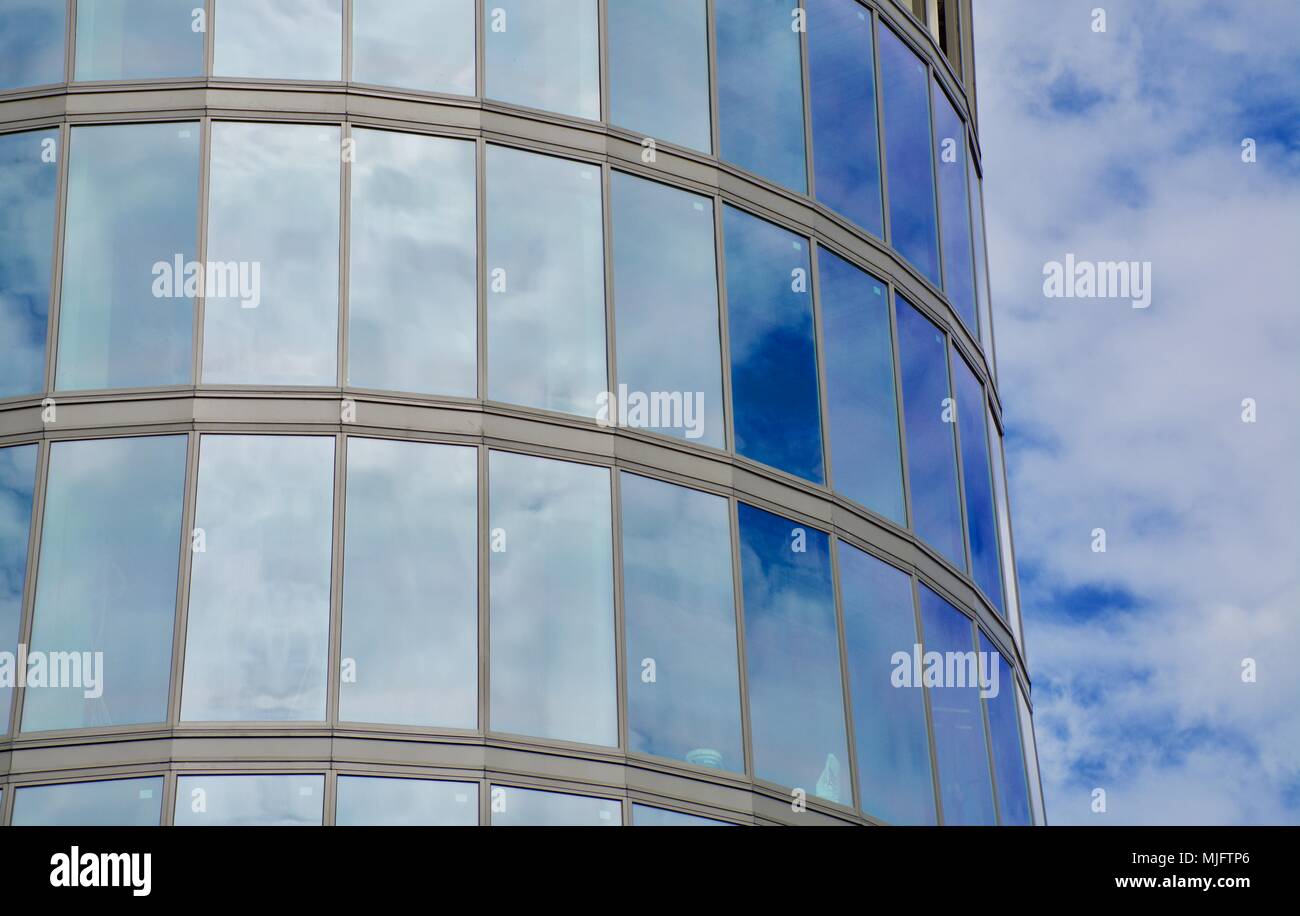 Costruzione di un nuovo cilindrico di vetro alto edificio con gru contro un nuvoloso cielo blu Foto Stock