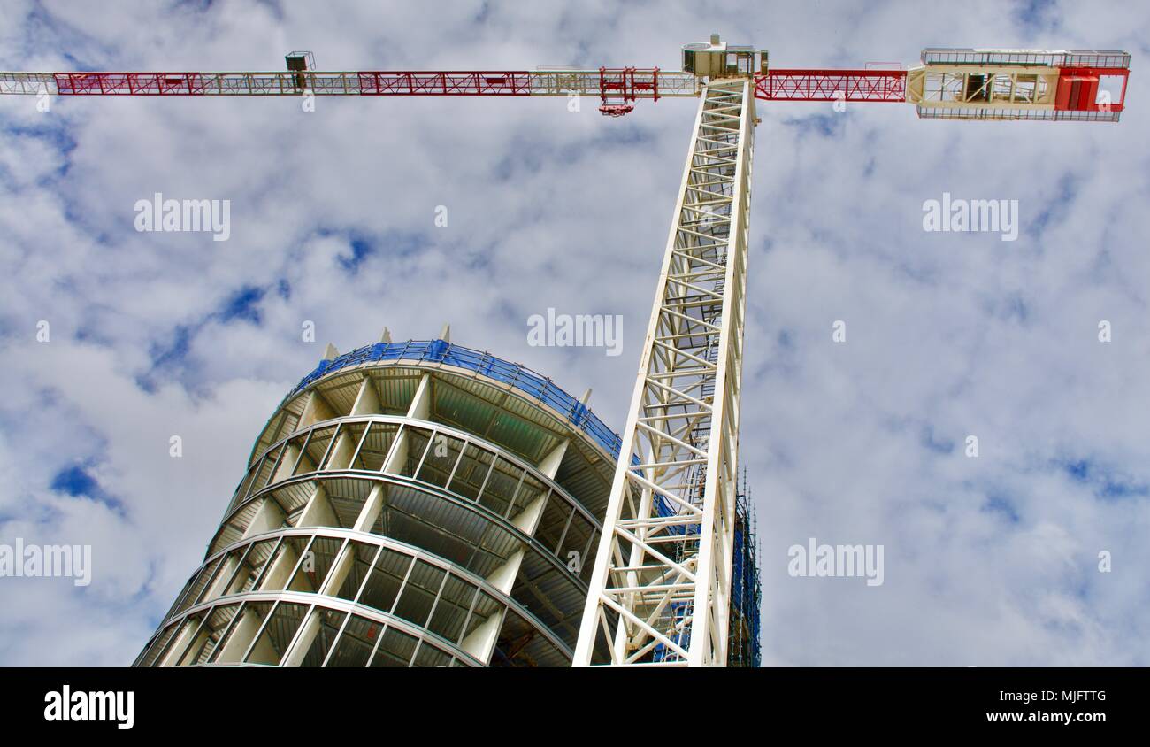 Costruzione di un nuovo cilindrico di vetro alto edificio con gru contro un nuvoloso cielo blu Foto Stock