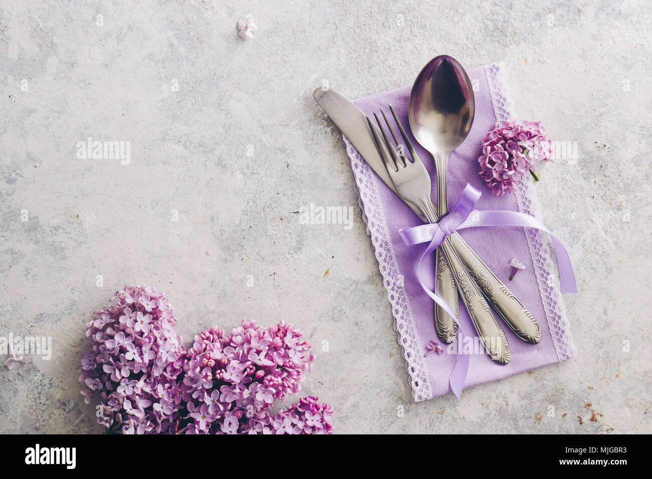 La molla della decorazione della tavola con fiori lilla. Elegante messa in tavola con fiori lilla, viola igienico e argenteria vintage su sfondo rustico. Foto Stock