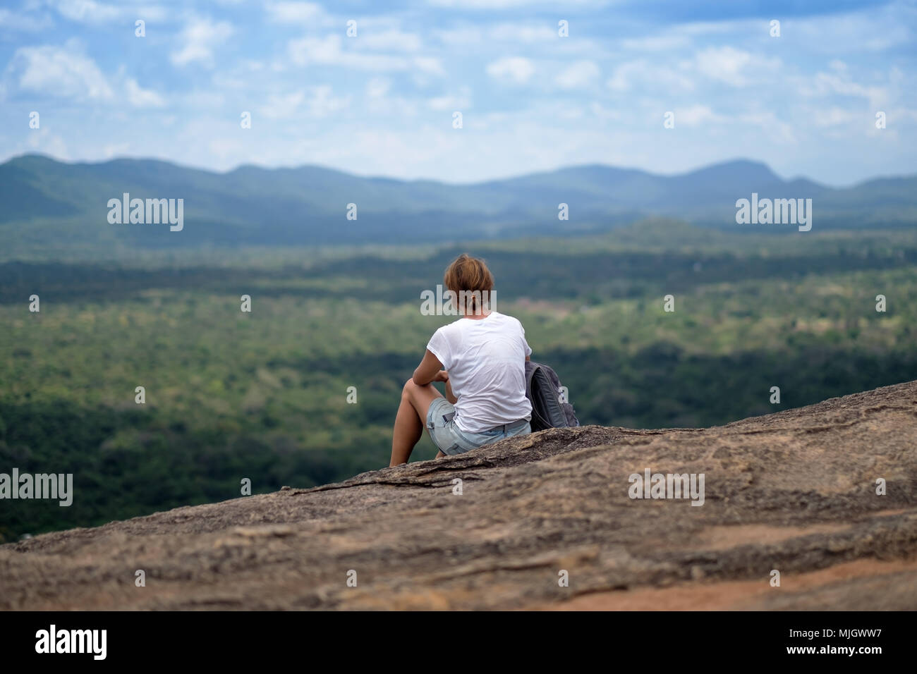 Giovane donna con zaino seduto sulla montagna e in cerca di un cielo di nuvole. La splendida natura dello Sri Lanka Foto Stock