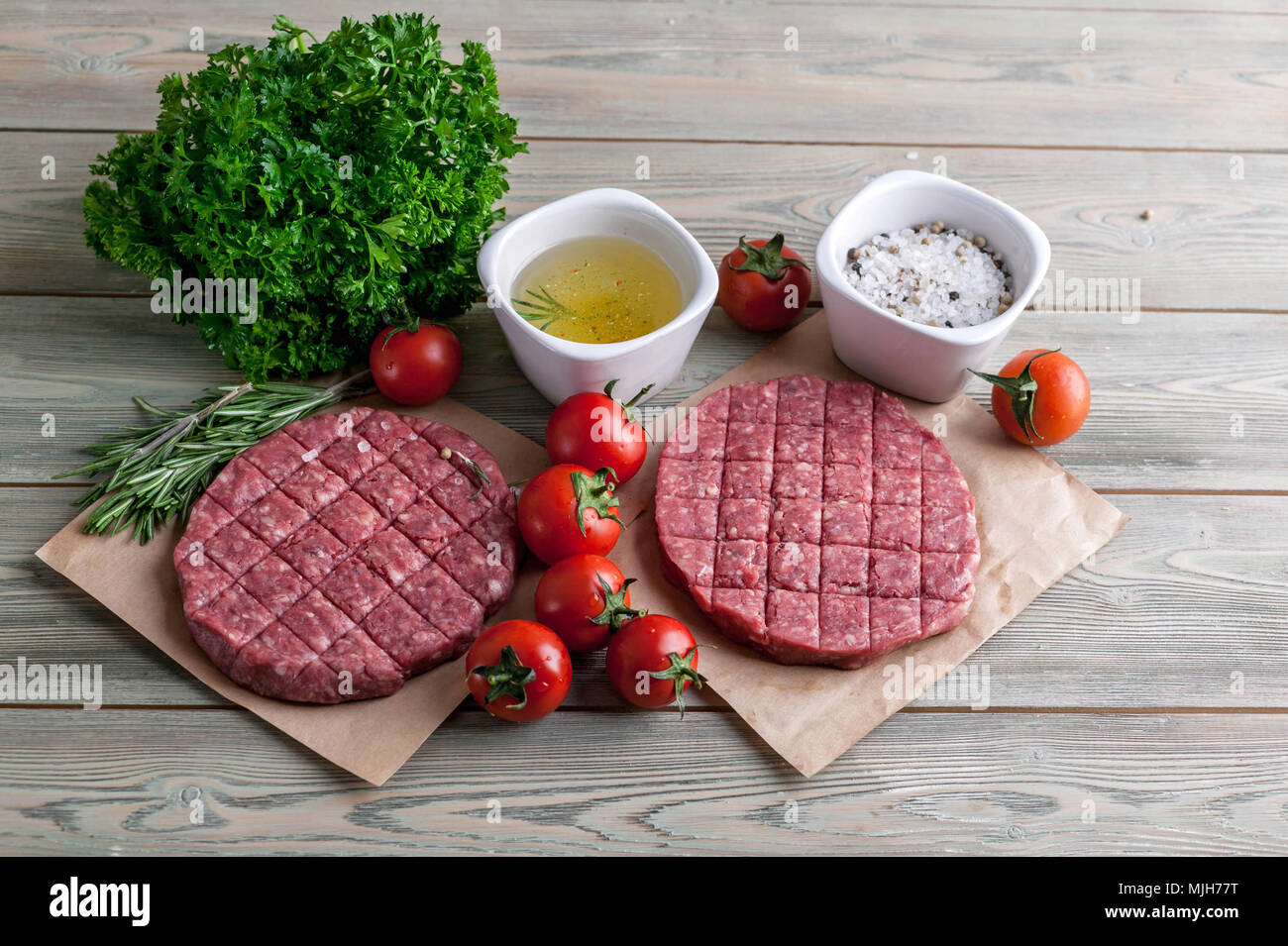 Cotolette di hamburger di carne fresca macinata con spezie fine erbe su una tavola di legno Foto Stock