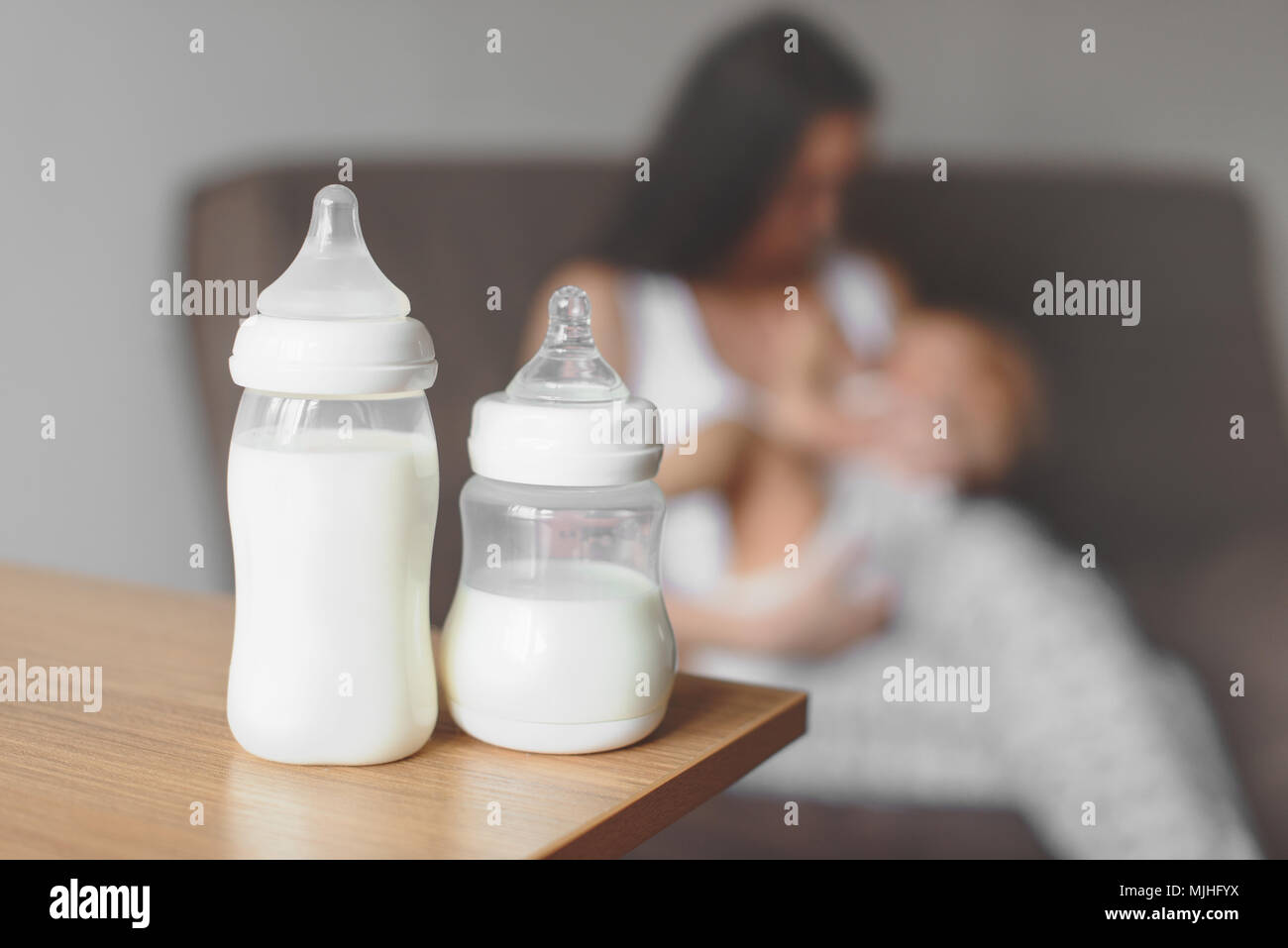 Le bottiglie con il latte materno sullo sfondo della madre tiene nelle sue mani e in allattamento neonato. La maternità e la cura del bambino. Foto Stock