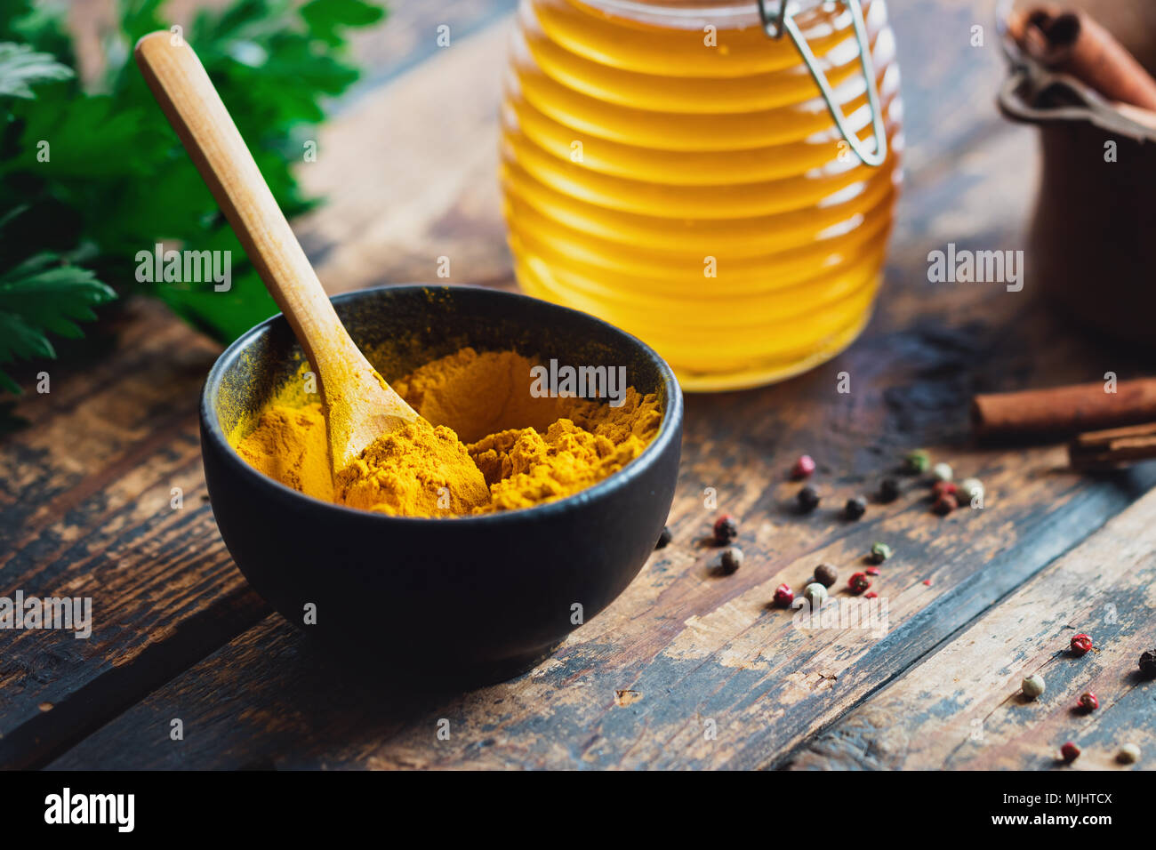 Curcuma in polvere in un recipiente nero con spezie su tavola in legno rustico Foto Stock