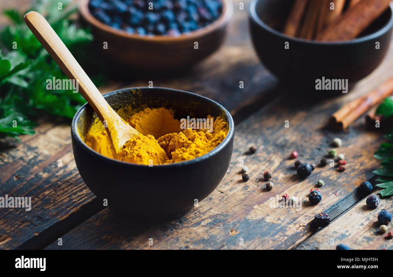 Curcuma in polvere in un recipiente nero con spezie su tavola in legno rustico Foto Stock