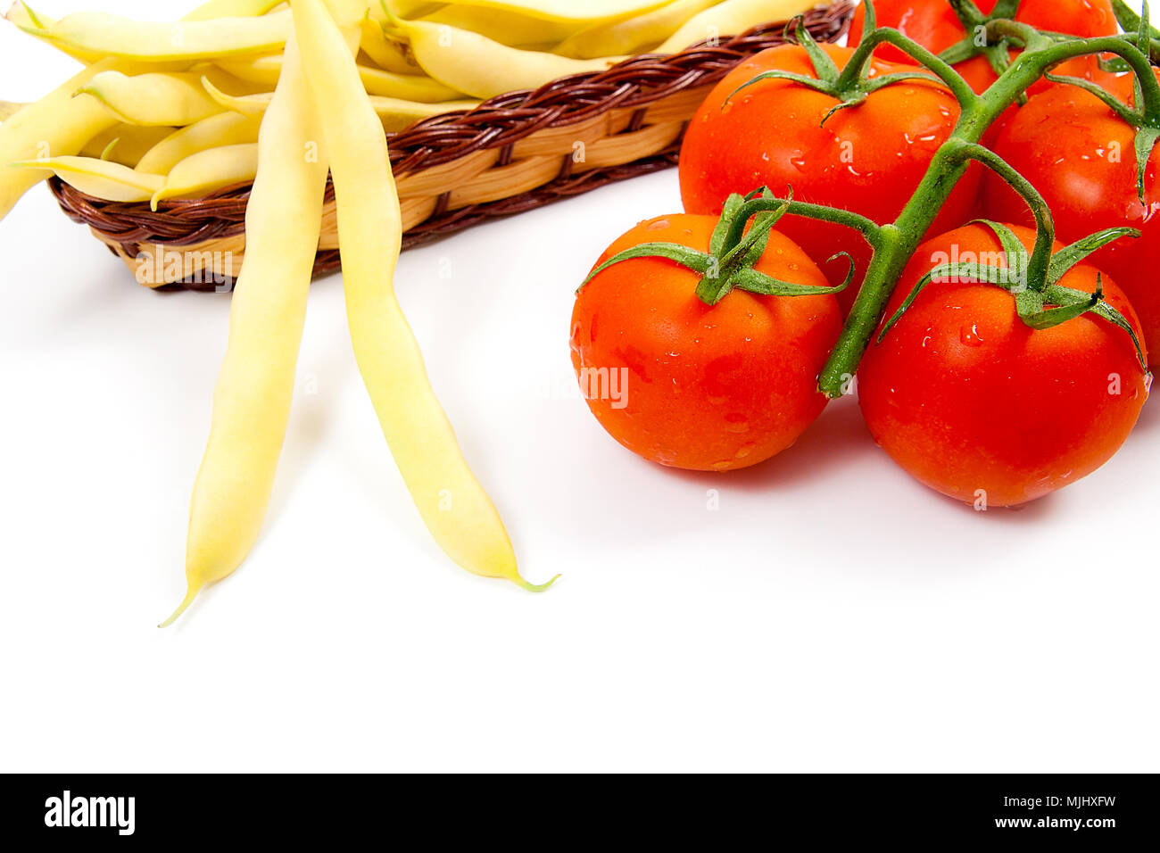 Giallo cesto in legno con giovani baccelli di fagioli con fagioli e il mazzetto di fresca di pomodori rossi con gocce d'acqua isolati su sfondo bianco Foto Stock