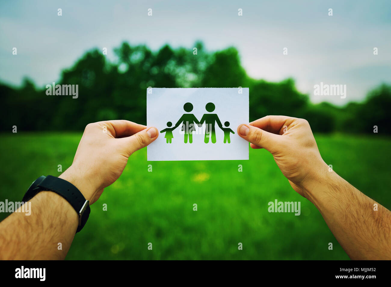 L'uomo mani tenendo un foglio bianco con silhouette simbolo, compreso padre, madre e due figli. Famiglia di assicurazione concetto isolato su un verde Foto Stock