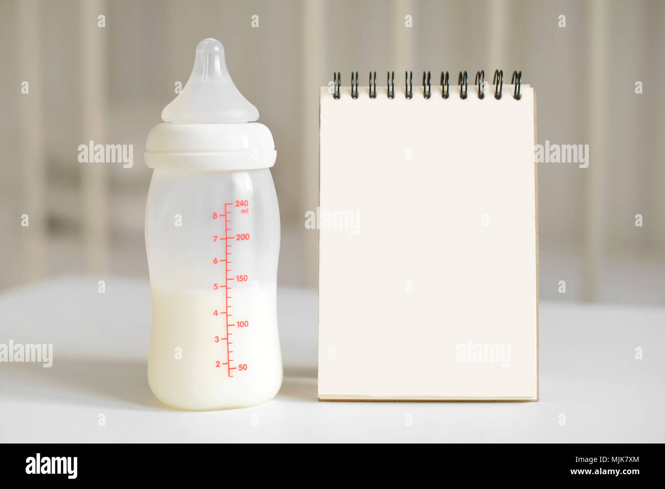 Bottiglia con il latte per il bambino e vuoto notepad sullo sfondo del letto per bambino. I neonati e i bambini del concetto. Copia gratuita dello spazio. Foto Stock